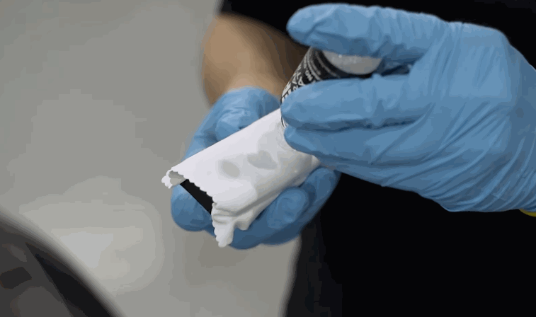 Blue-gloved hands squeezing ceramic coating liquid onto an applicator pad before treating a car’s paintwork in Chesterfield, MO.