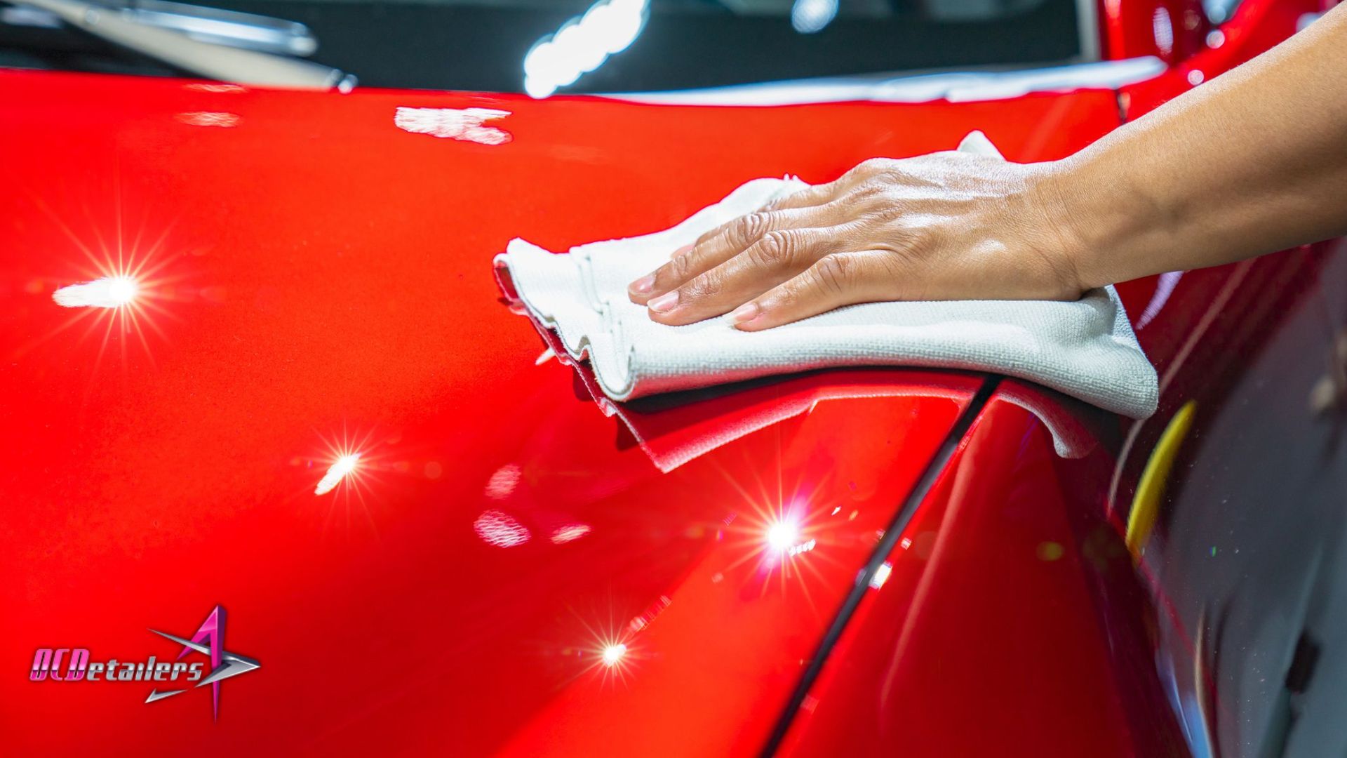 Hand buffing a vibrant red car to a mirror-like shine after ceramic coating application in Chesterfield, MO, reflecting bright workshop lights.