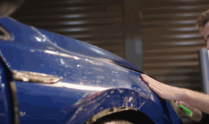 Paint protection film being trimmed and fitted along the hood edge of a blue car.