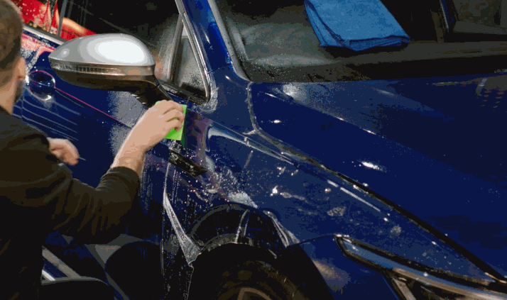 Installer pressing paint protection film onto the side of a blue SUV with a green applicator.