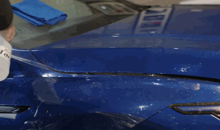 Technician carefully stretching paint protection film over a blue vehicle’s fender.