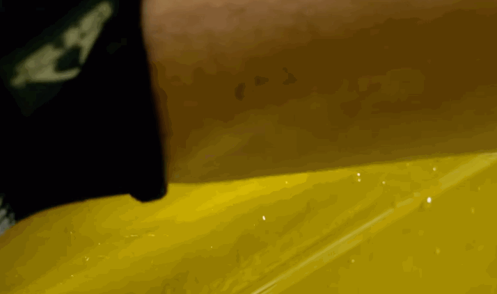Detailer smoothing yellow paint protection film across a vehicle hood to ensure a seamless fit.