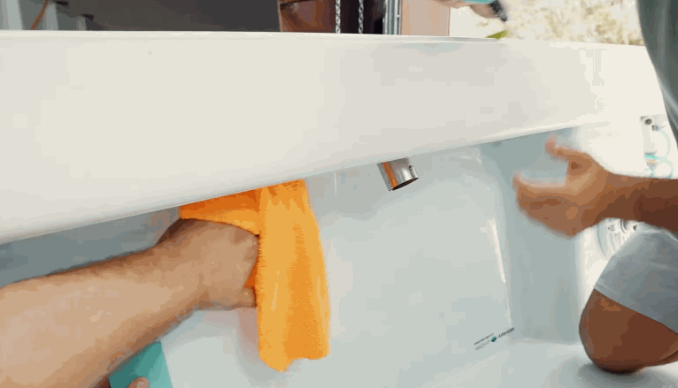Two people working together to smooth and dry the underside of a boat’s rear section, one using a microfiber cloth and the other holding a blue applicator tool.
