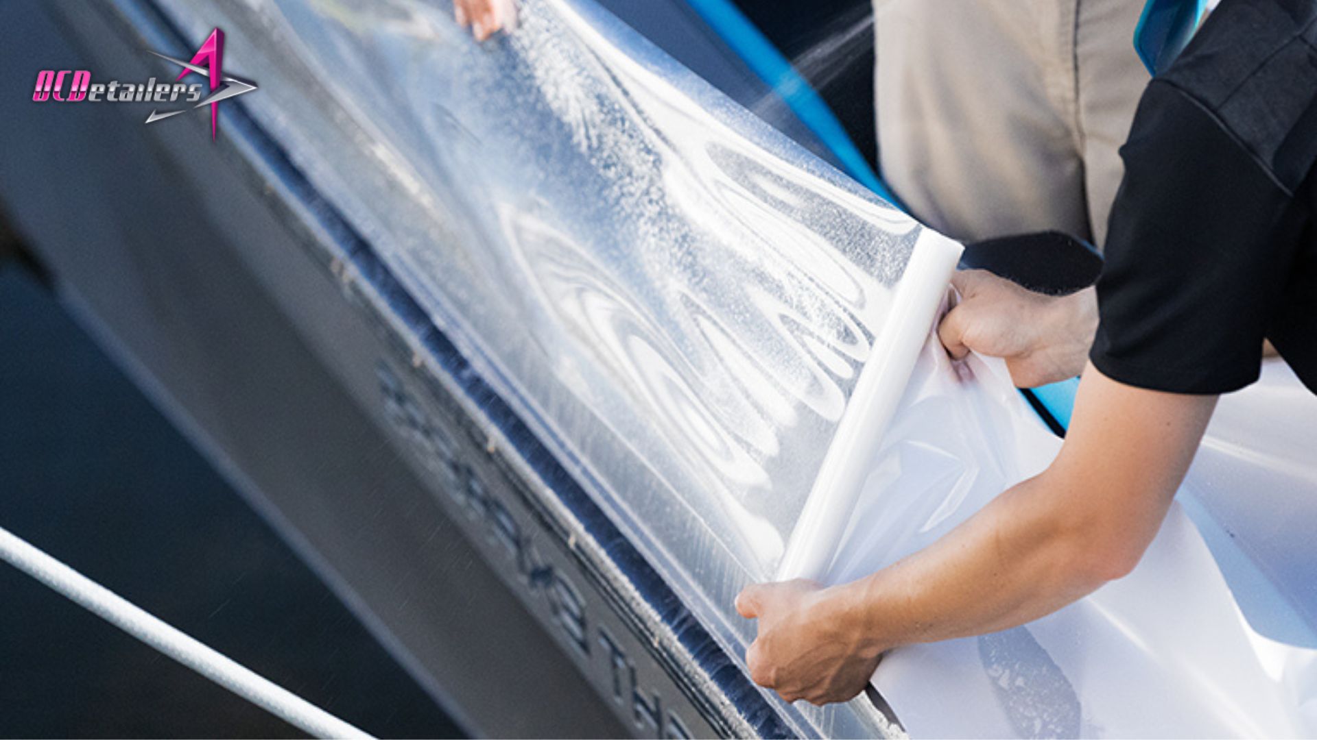 Person spraying water and applying a large sheet of PPF along the side of a docked boat.