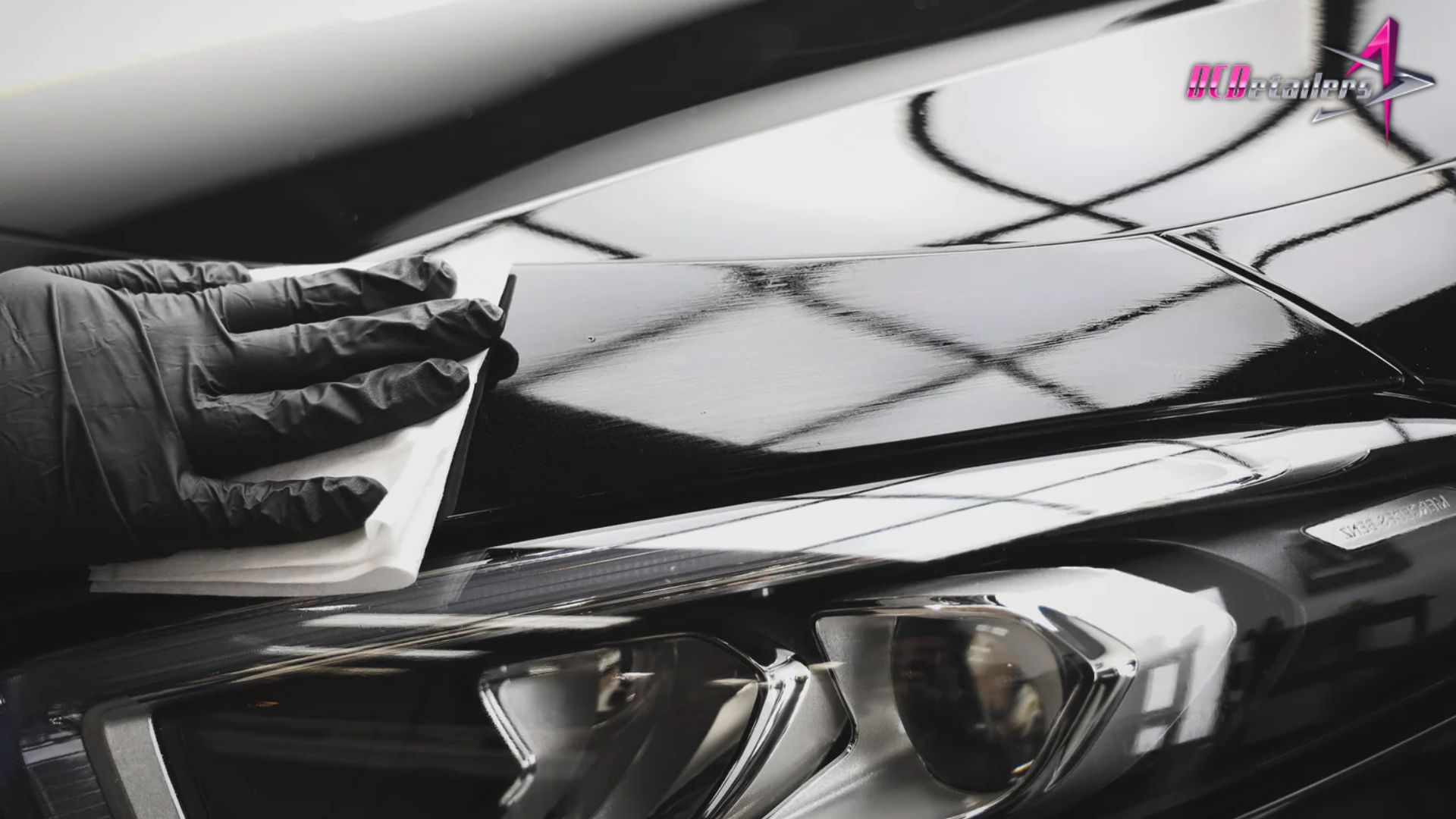 Detailer in black gloves applying ceramic coating to a car’s hood with a microfiber cloth.