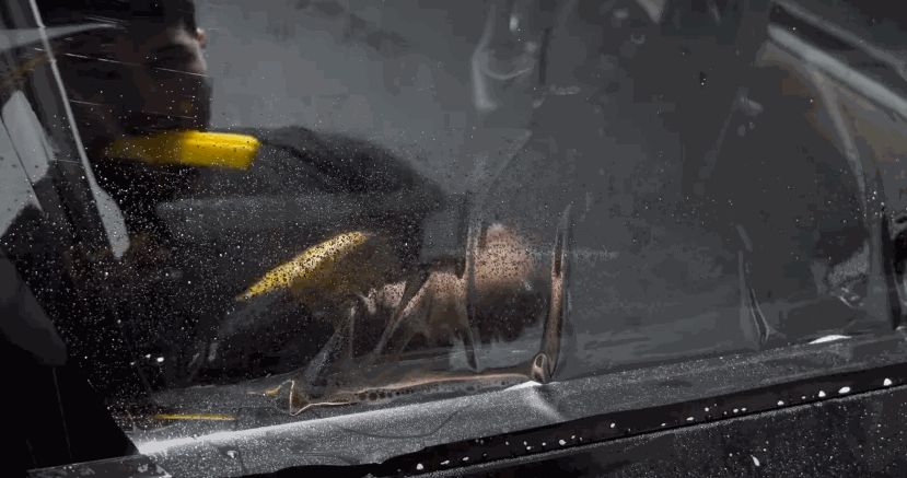 Worker using a squeegee to press and smooth new window tinting film onto a wet car window.