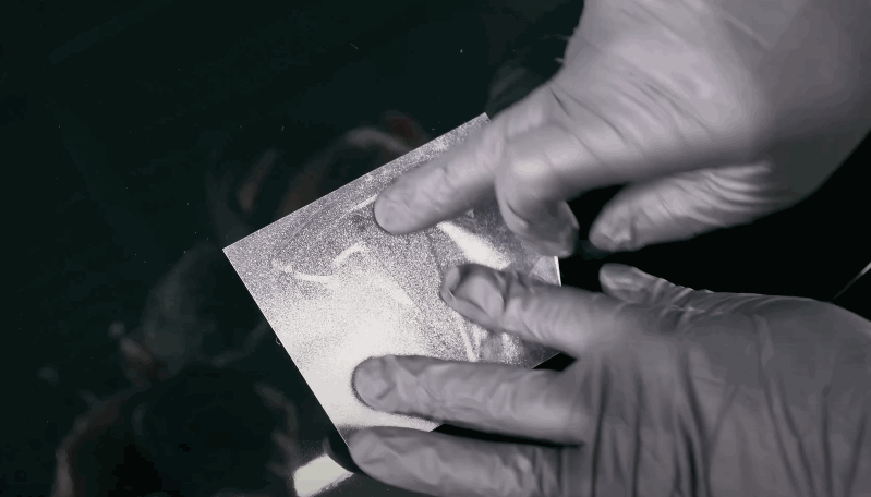 Hands in gloves testing the smooth surface of a coated car panel with a small sample square.