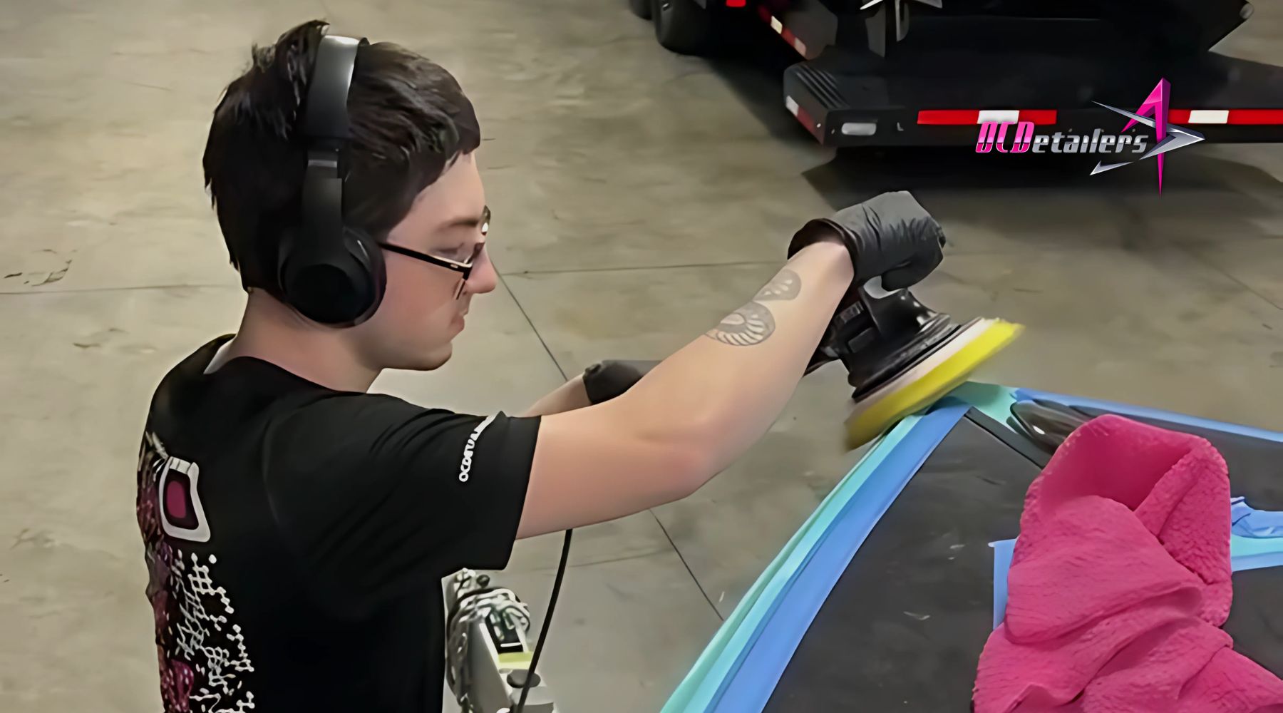 A detailer in a black shirt and gloves performs Marine Ceramic Coating Maintenance on a boat at a garage in Osage Beach, using a dual-action polisher near a windshield taped off with painter's tape. A bright pink microfiber towel is folded on the boat's surface, emphasizing a careful and professional detailing process.