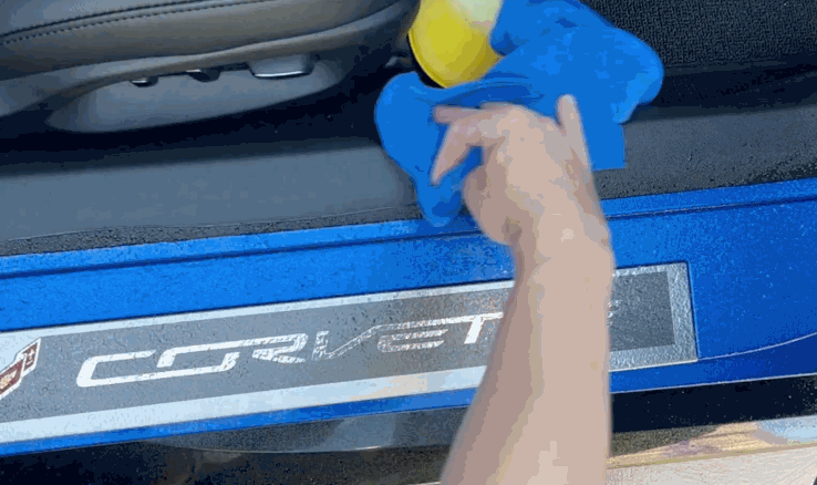 Detailing a Corvette interior door sill with a blue microfiber cloth and yellow pad to prep the surface before installing paint protection film.