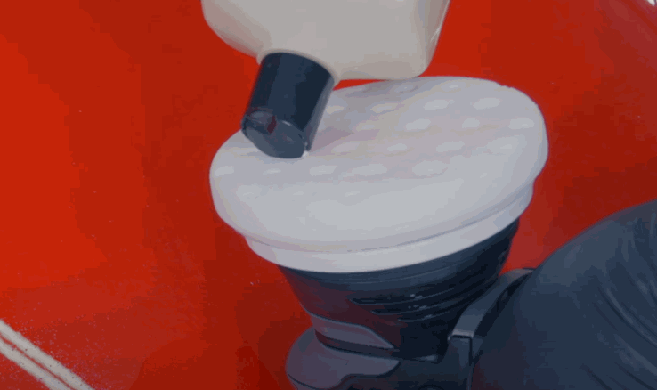 A white foam pad on a polishing machine is being primed with ceramic coating compound over a red car panel.