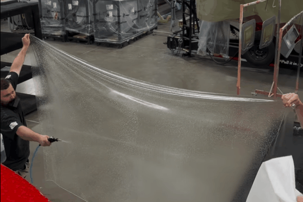 An OCDetailers professional installer applying paint protection film to the hood of a red car.