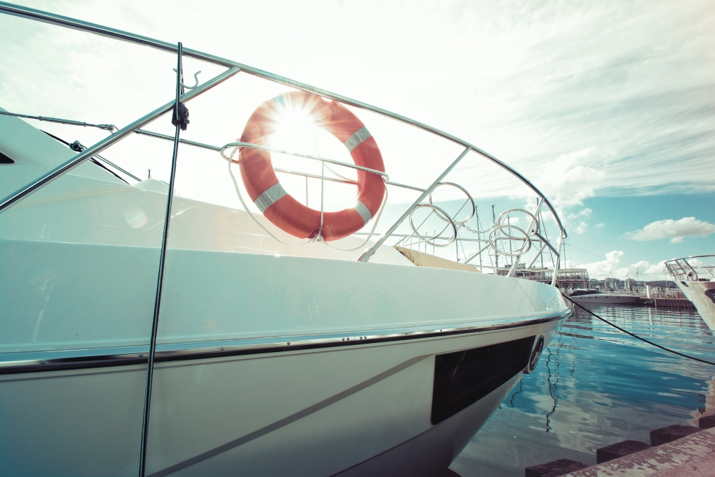 A sleek white boat docked at a marina in Osage Beach with the sun shining through a red and white life ring. The image highlights the exposed hull, illustrating why The Role of PPF is essential for protecting against sun damage, docking wear, and lake debris.